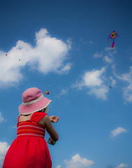 A girl in a red dress flying a kite on a cloudy day.
