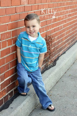 A young boy standing in front of a brick building posing for Kitty Vogt Photography.