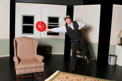 A man with a red balloon on stage performing Balloonacy at the Rose Theater.