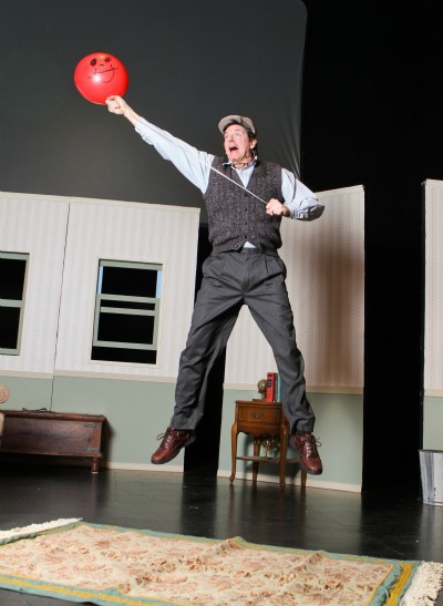 A man jumping in the air with a red balloon on stage performing Balloonacy at the Rose Theater.