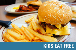 A large sandwich and fries on a plate with overlay text that reads Kids Eat Free