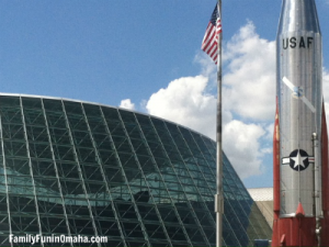 A US flag flying over a glass building at SAS Museum for the Omaha Photo Scavenger Hunt for kids.