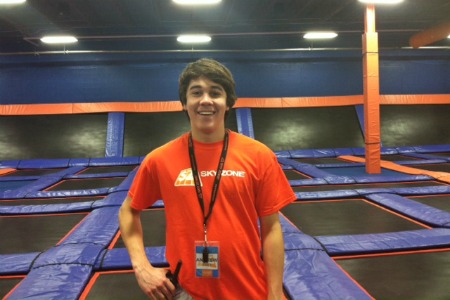 A young man in a SkyZone shirt standing in front of trampolines at Sky Zone Omaha Trampoline Park.