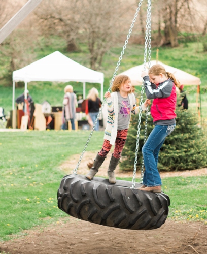 Girls standing on a tire swing at Bloom Where You\'re Planted Farm.