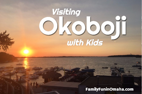 A sunset over a body of water and boat dock with overlay text that reads Visiting Okoboji with Kids