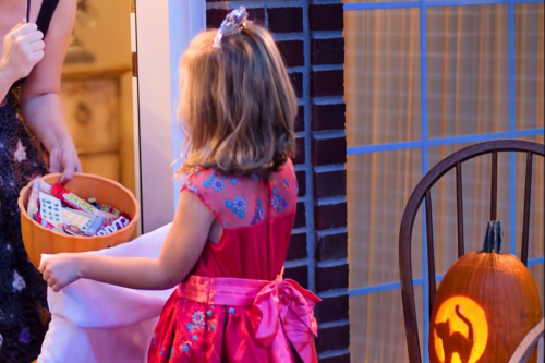A little girl standing in front of a bowl of Halloween treats.