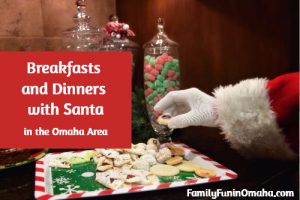 A close up of Santa taking a cookie of a tray with overlay text that reads, \"Breakfasts and Dinners with Santa in Omaha.\"