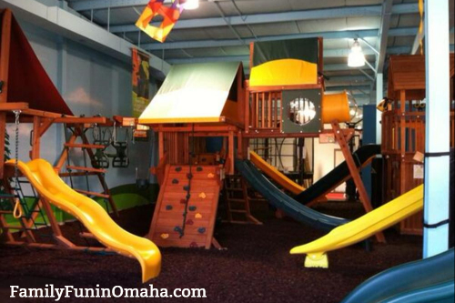 A large wooden playset inside of a building at Backyard Playworld. 