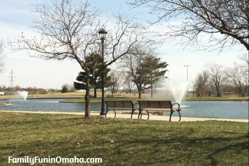 Trees and benches next to a pond and fountain at Halleck Park in Omaha