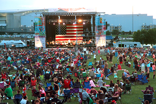 A group of people sitting on a lawn in front of a stage of musicians.