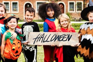 A group of children in costumes holding a Halloween sign