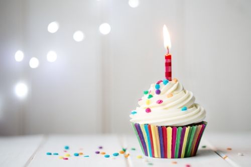 A close up of a colorful cupcake with a lit candle.